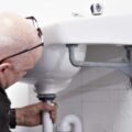 A person is fixing or installing a u-bend pipe under a white ceramic wash basin