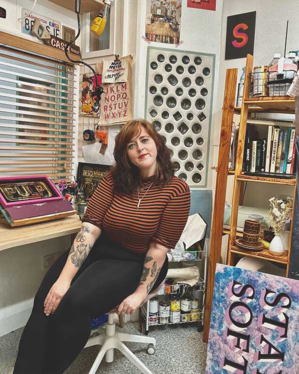 Image shows Abbi sitting in her sign painting studio