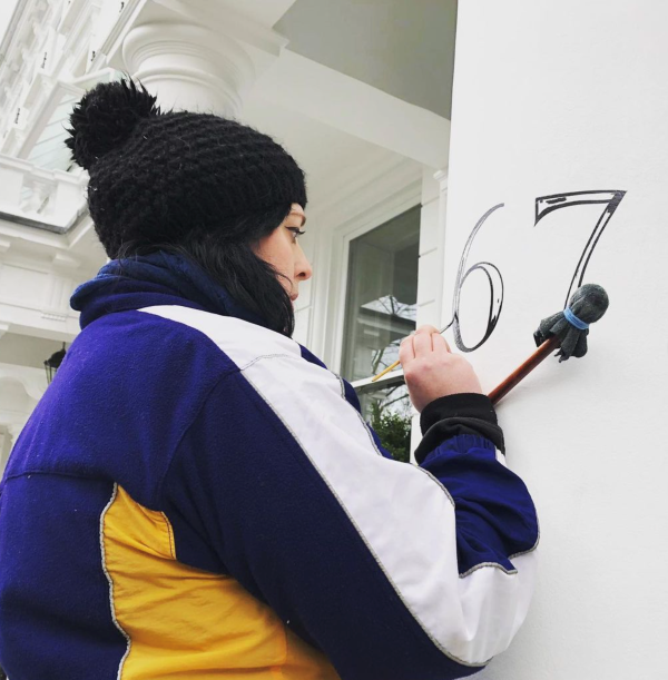 Image shows Abbi painting numbers onto a building.