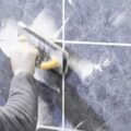 Image shows blue ceramic wall tiles with grout being applied. A hand is moving the grout float across the tiles to apply the grout